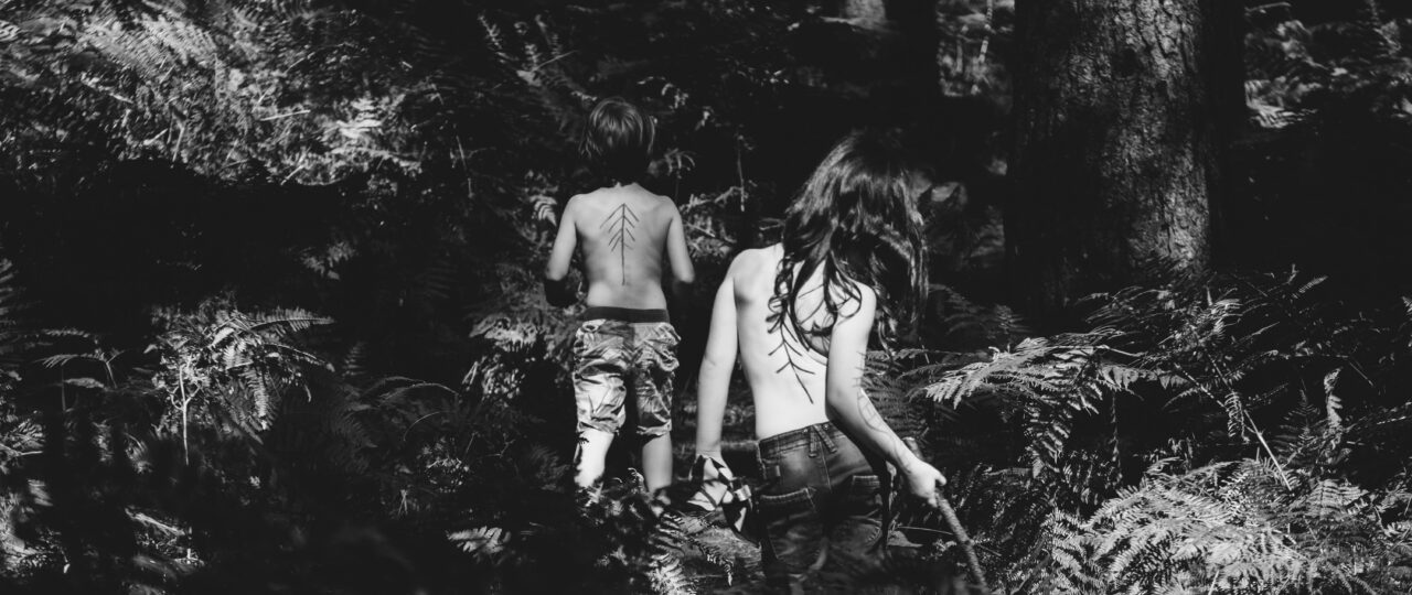 grayscale photography of two topless persons standing at the forest during day